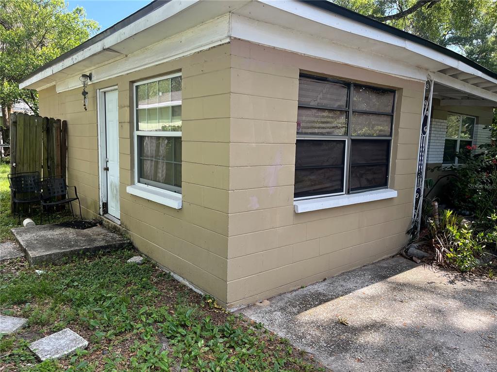 A tan concrete block house exterior with a white door and metal-framed windows — 3104 E CHELSEA STREET, TAMPA, FL