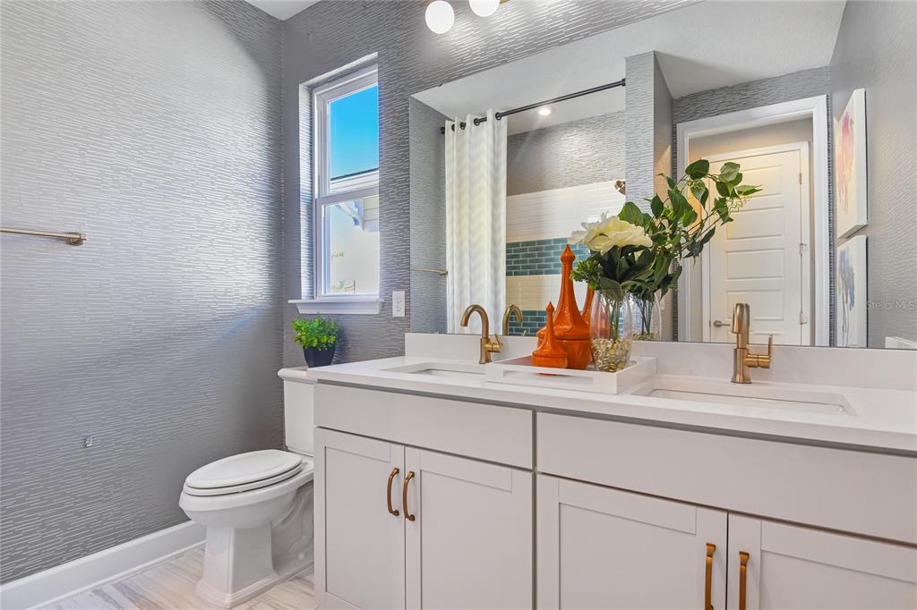 A bathroom features a double vanity with gold fixtures, gray textured wallpaper, and a window — 231 THORNBERRY WAY, PALM COAST, FL
