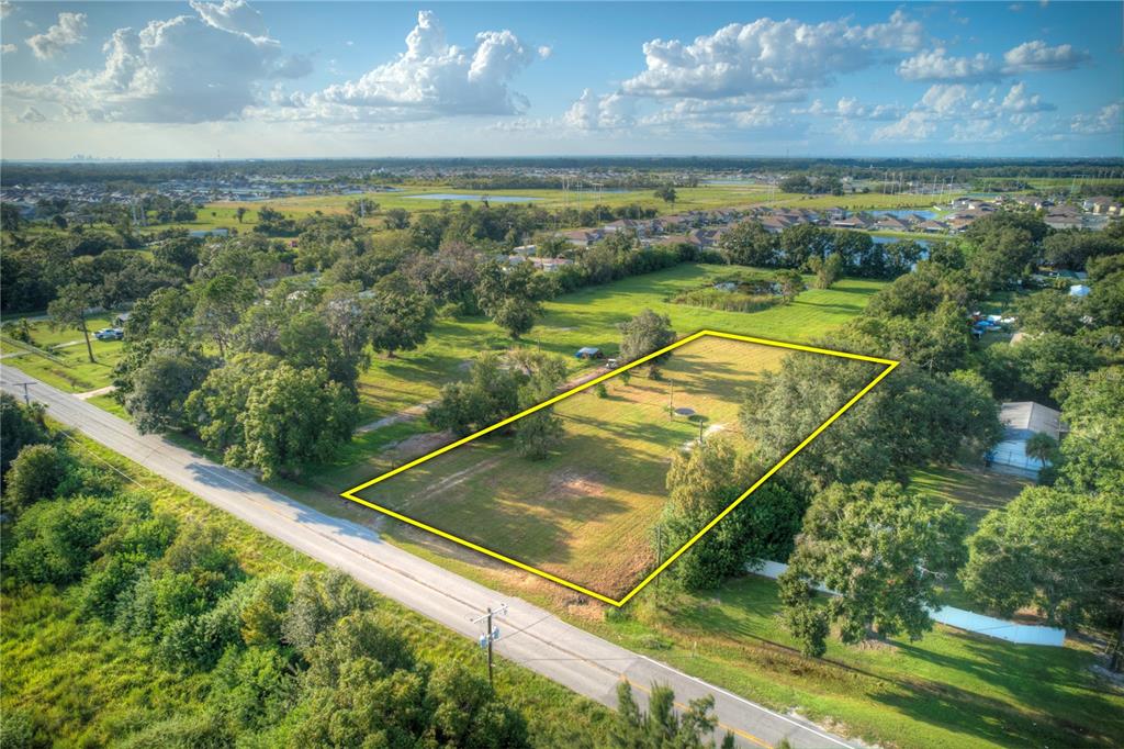 An aerial view shows a rectangular, grassy vacant lot outlined in yellow beside a road — 1520 21ST AVENUE SE, RUSKIN, FL