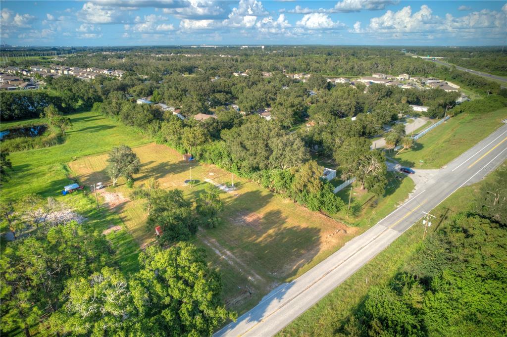 An aerial view shows a vacant, grassy lot bordered by trees and a paved road — 1520 21ST AVENUE SE, RUSKIN, FL