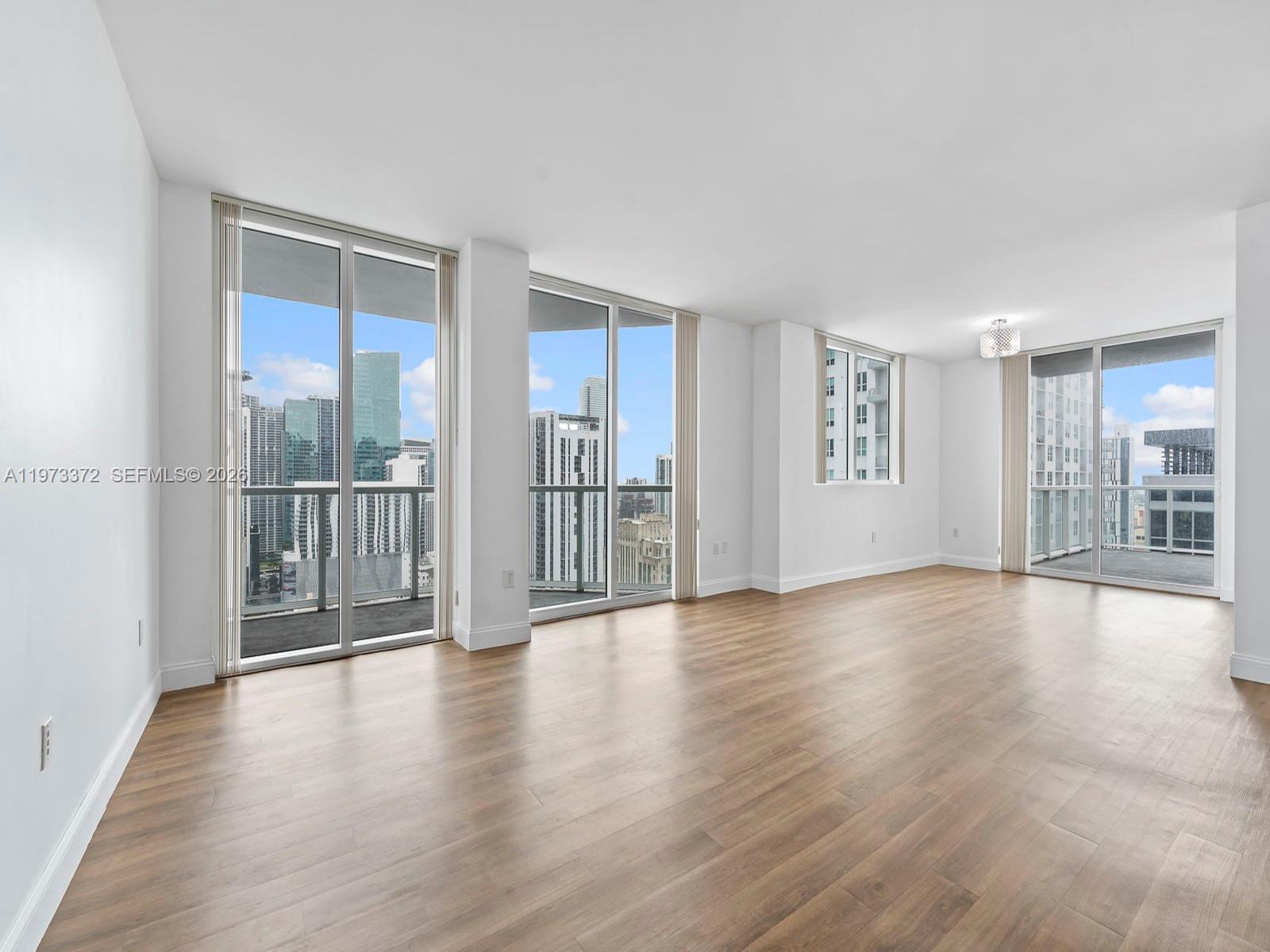 An empty room with wood-look flooring, white walls, and floor-to-ceiling windows overlooking a city skyline — 253 NE 2nd St # 3108, Miami FL 33132, MIAMI, FL