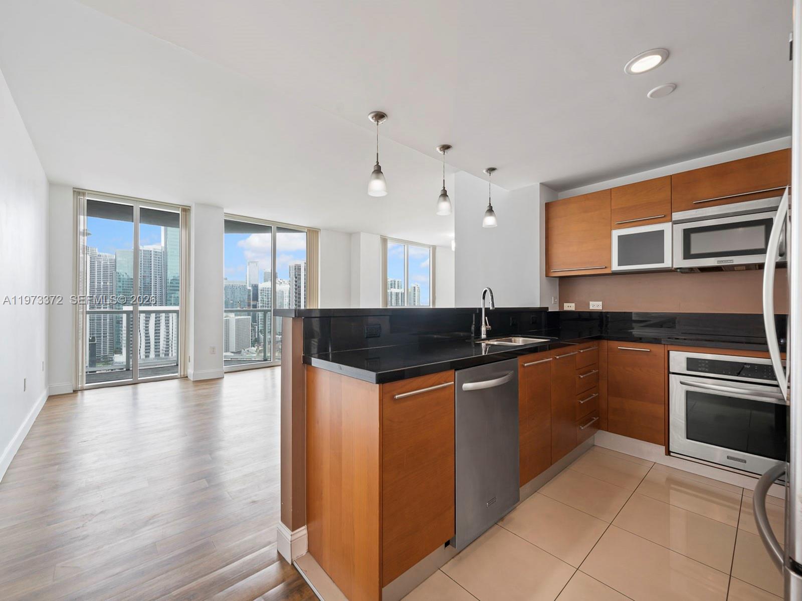 A modern kitchen with wood cabinets and black countertops overlooks a living area with city views — 253 NE 2nd St # 3108, Miami FL 33132, MIAMI, FL