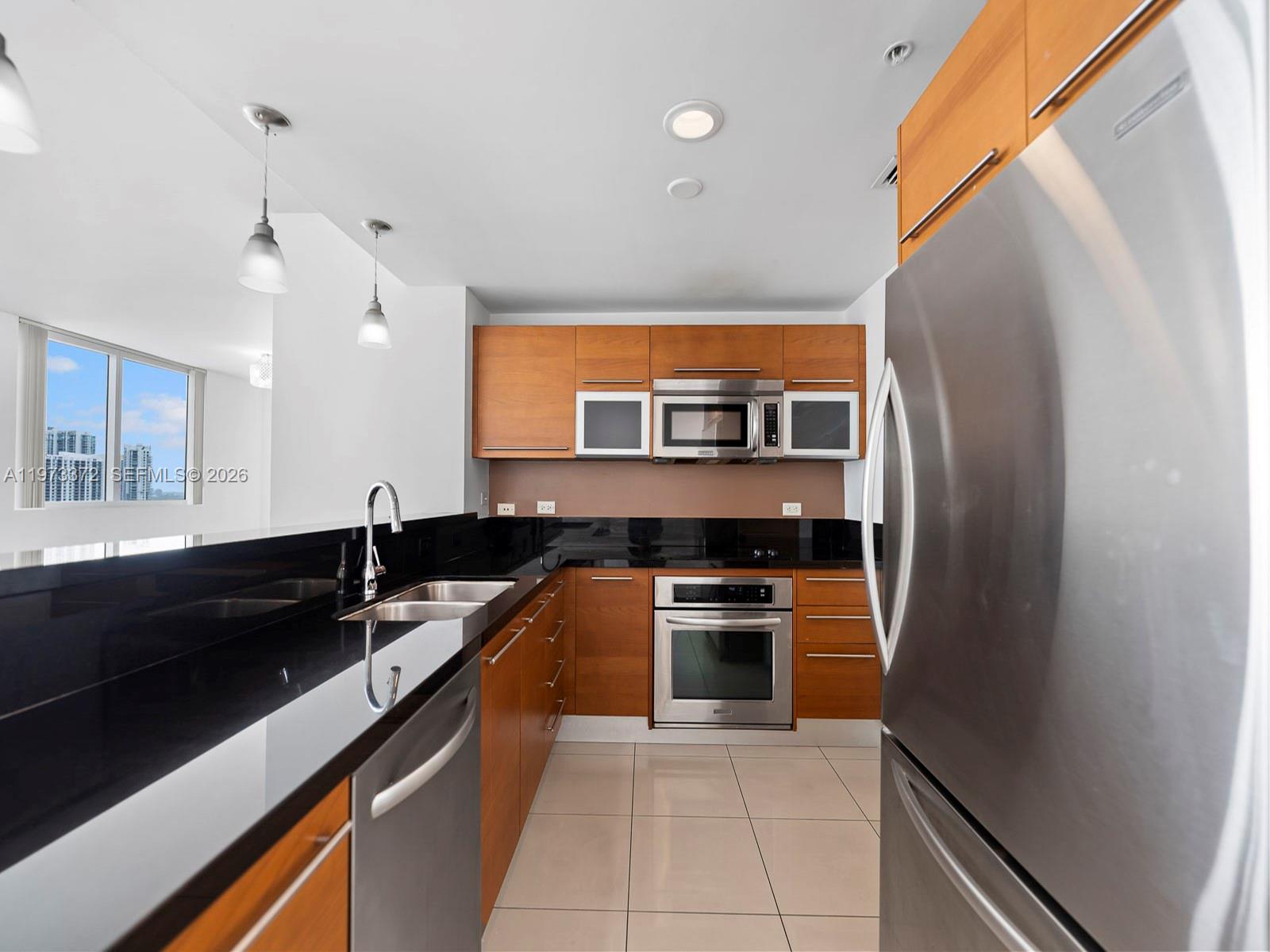 A modern kitchen features wood cabinets, stainless steel appliances, and black countertops — 253 NE 2nd St # 3108, Miami FL 33132, MIAMI, FL