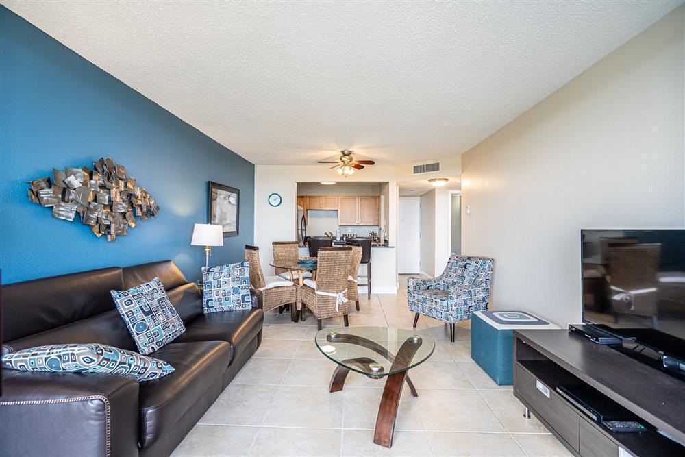 A living room with a blue accent wall, leather sofa, glass coffee table, and dining area — 1830 Embassy Drive # 409, West Palm Beach FL 33401, WEST PALM BEACH, FL
