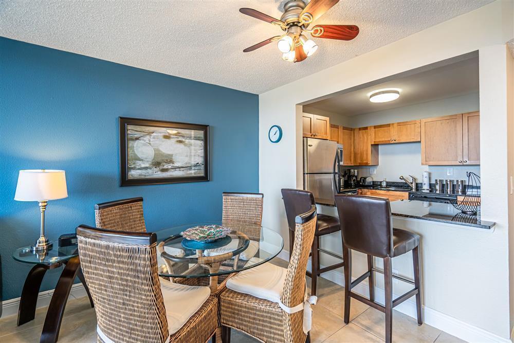 A dining area with a glass table and wicker chairs sits next to a kitchen — 1830 Embassy Drive # 409, West Palm Beach FL 33401, WEST PALM BEACH, FL