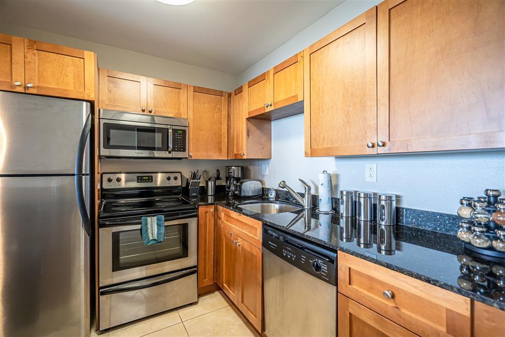 A kitchen features light wood cabinets, stainless steel appliances, and dark granite countertops — 1830 Embassy Drive # 409, West Palm Beach FL 33401, WEST PALM BEACH, FL