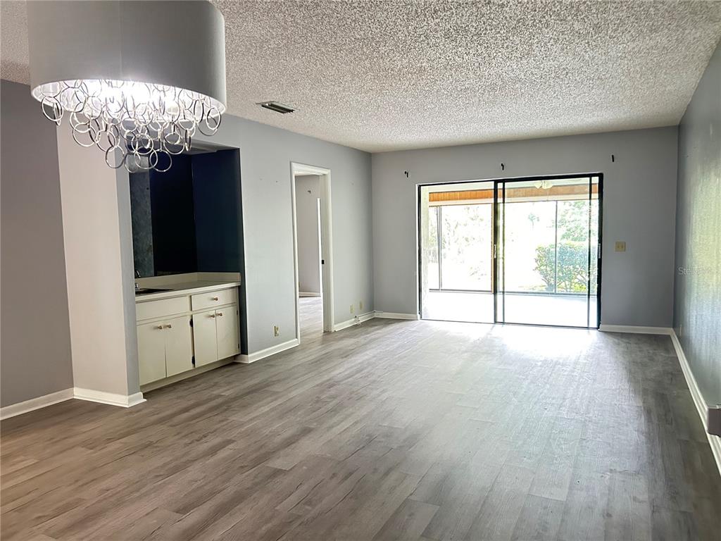 A living room features gray walls, wood-look flooring, a wet bar, and sliding glass doors — 1026 MEDINAH DRIVE, WINTER HAVEN, FL