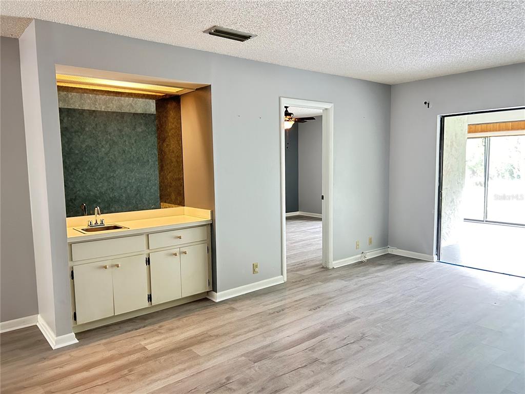 A room with light gray walls, wood-look flooring, a wet bar, and a sliding glass door — 1026 MEDINAH DRIVE, WINTER HAVEN, FL