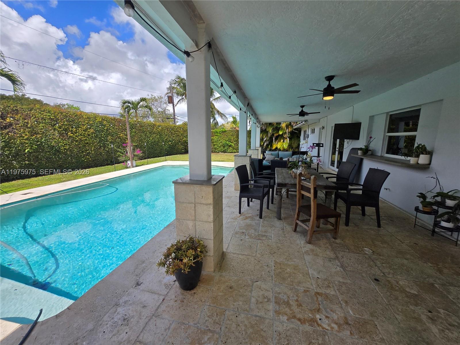 A covered patio with stone flooring overlooks a swimming pool and a manicured hedge — 8620 SW 85th Ave, Miami FL 33143, MIAMI, FL