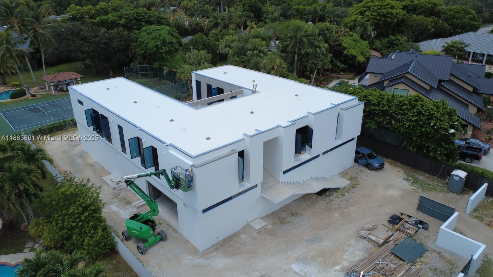 An aerial view shows a modern white U-shaped house under construction with a green boom lift — 13050 SW 103 Ave, Miami FL 33176, MIAMI, FL