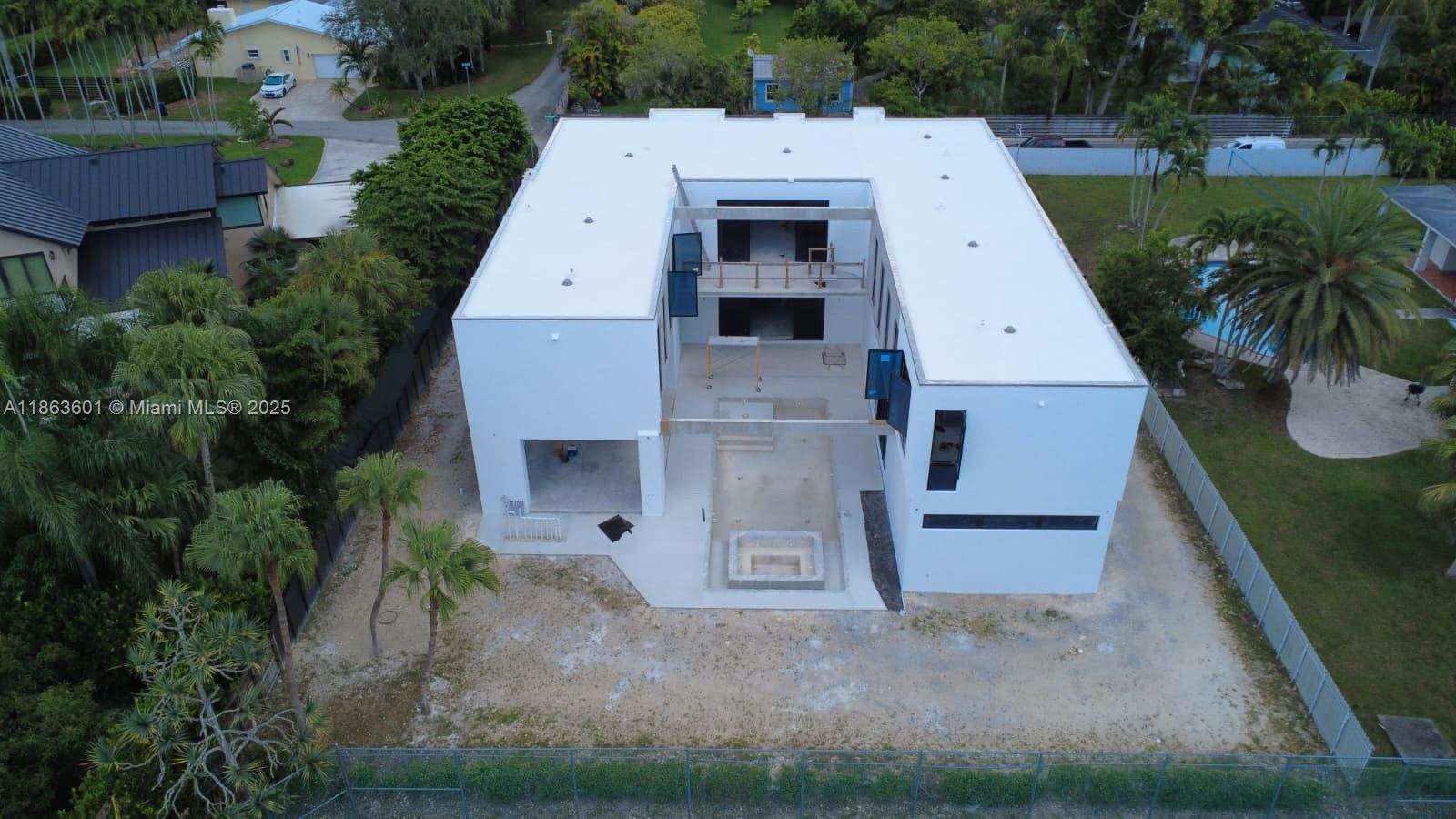 An aerial view of a modern, U-shaped white house under construction with an unfinished pool area — 13050 SW 103 Ave, Miami FL 33176, MIAMI, FL
