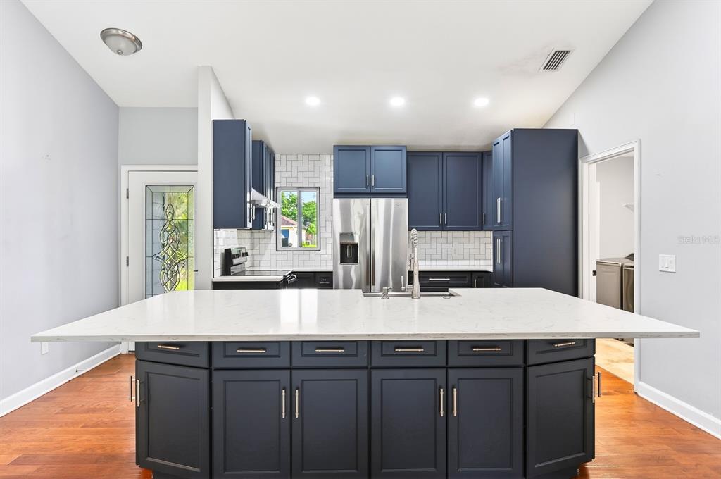 A kitchen features dark blue cabinets, a large white quartz island, and stainless steel appliances — 116 W 5TH STREET, CHULUOTA, FL
