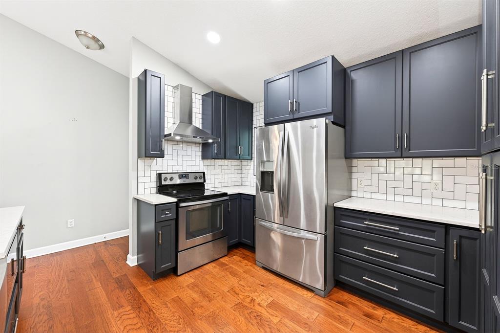A kitchen features dark blue cabinets, stainless steel appliances, white subway tile, and hardwood floors — 116 W 5TH STREET, CHULUOTA, FL
