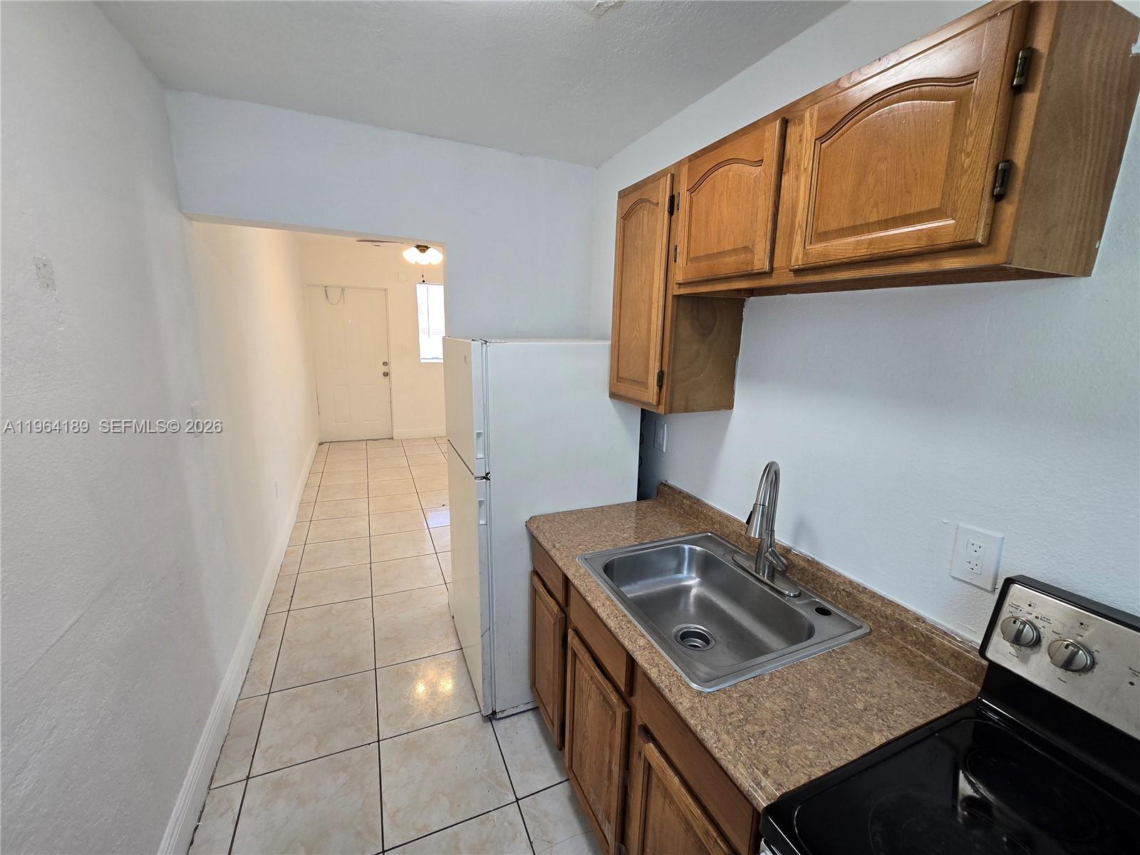 A small kitchen features wooden cabinets, a stainless steel sink, and a white refrigerator — 535 NW 7th St # 9, Miami FL 33136, MIAMI, FL