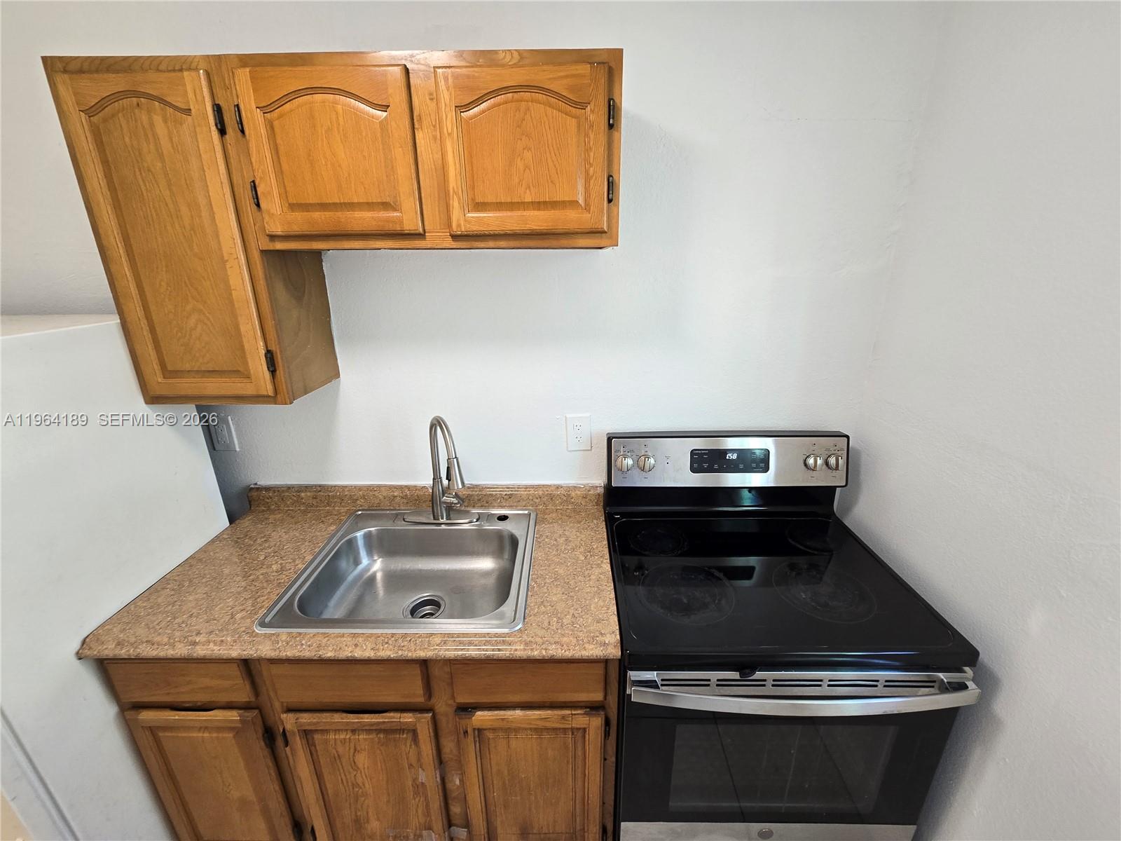 A small kitchen features wooden cabinets, a stainless steel sink, and a black electric stove — 535 NW 7th St # 9, Miami FL 33136, MIAMI, FL