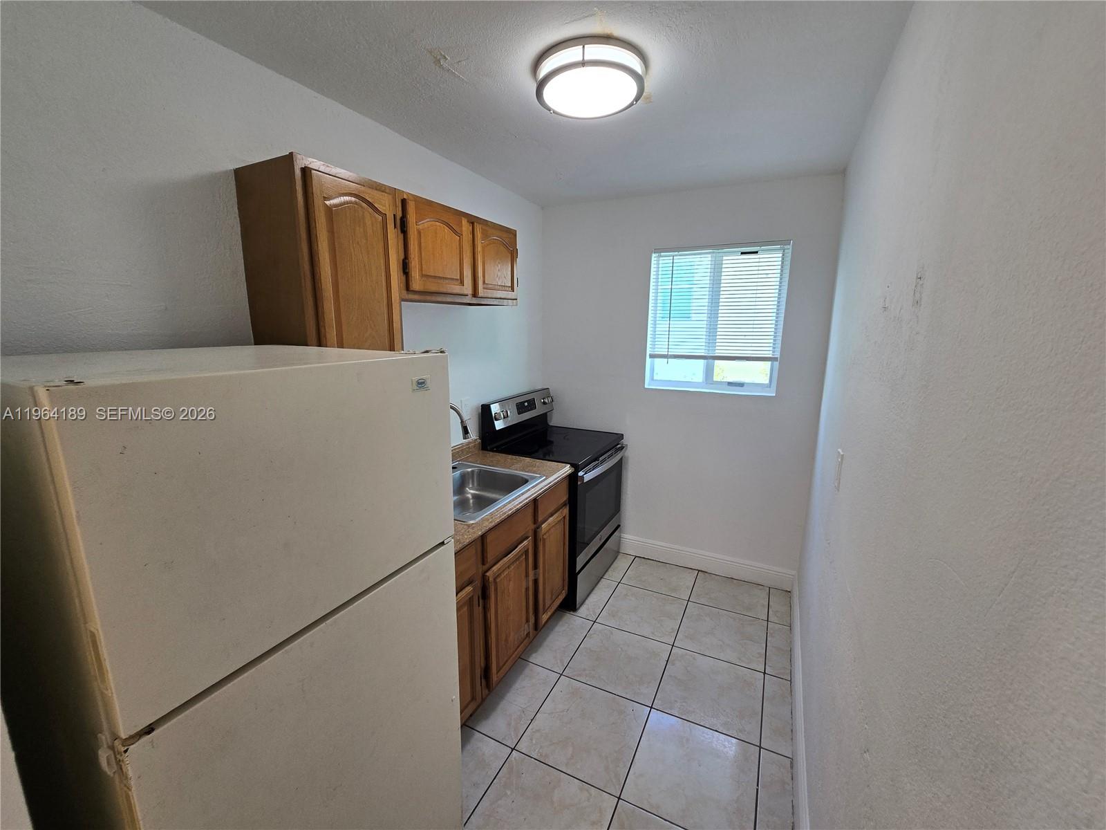 A small kitchen features white walls, tile flooring, wooden cabinets, and a black stove — 535 NW 7th St # 9, Miami FL 33136, MIAMI, FL