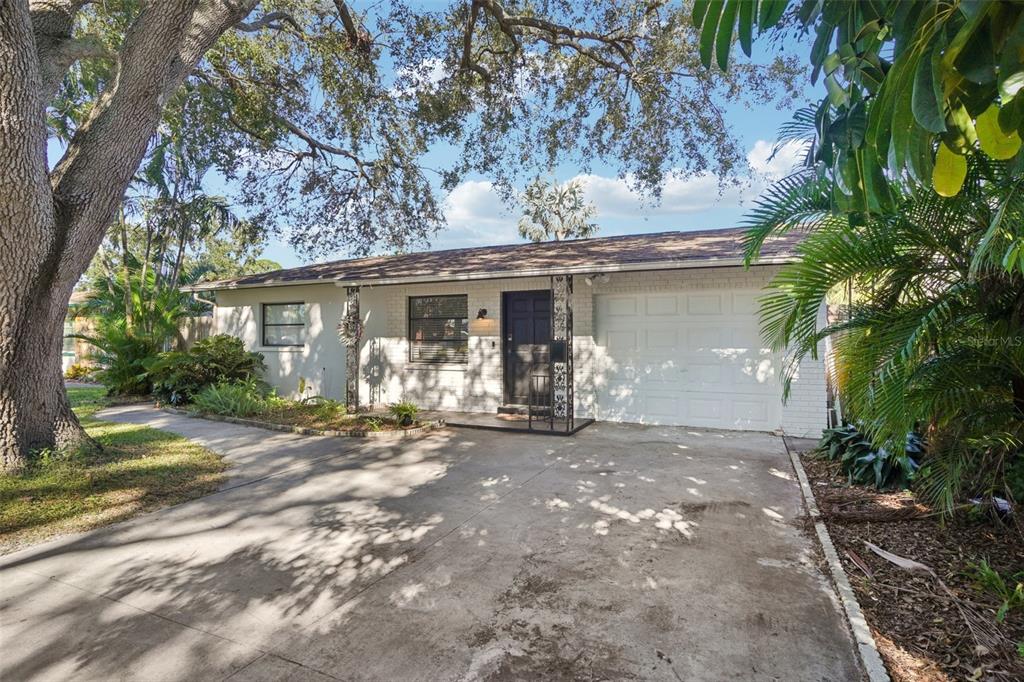 A single-story house with a white brick exterior, a concrete driveway, and a large tree — 162 SE LINCOLN CIRCLE N, ST PETERSBURG, FL
