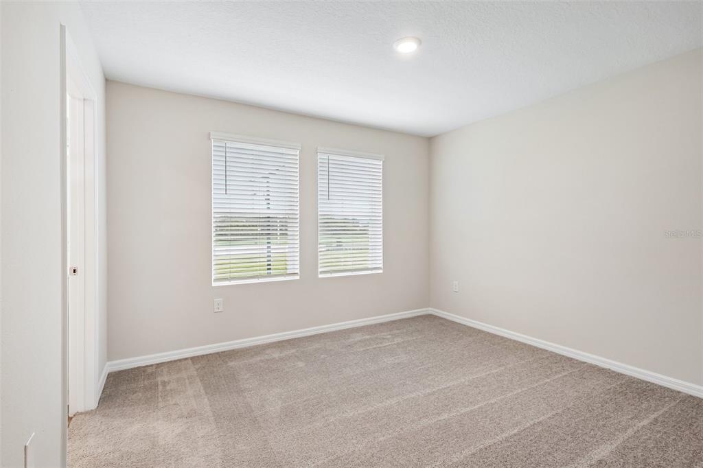 An empty bedroom features beige walls, carpeted flooring, two windows with blinds, and a ceiling light — 9176 BENT BRANCH, DADE CITY, FL