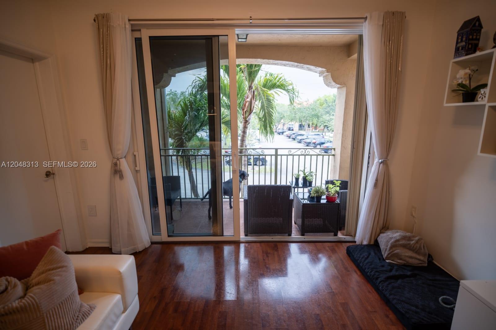 A living room with hardwood floors opens through sliding glass doors to a balcony with furniture — 6520 NW 114th Ave # 1626, Doral FL 33178, DORAL, FL