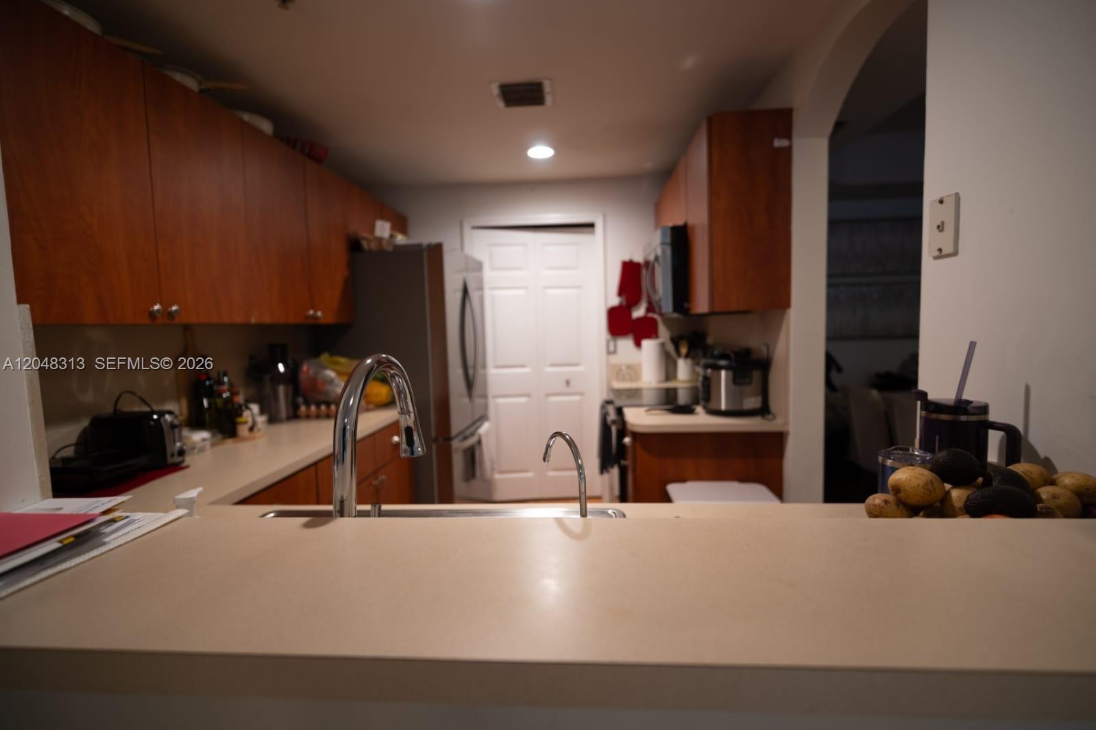 A kitchen features wood cabinets, light countertops, a stainless steel refrigerator, and a double sink — 6520 NW 114th Ave # 1626, Doral FL 33178, DORAL, FL