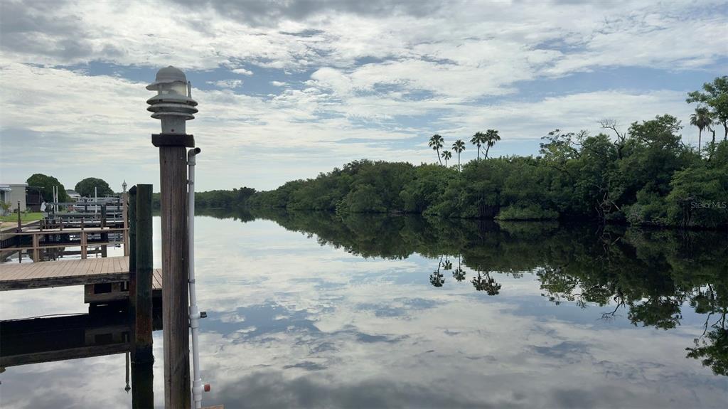 A wooden dock overlooks a calm canal lined with lush green trees and palm trees — 436 MOUNT OAK AVENUE NE UNIT 747, ST PETERSBURG, FL