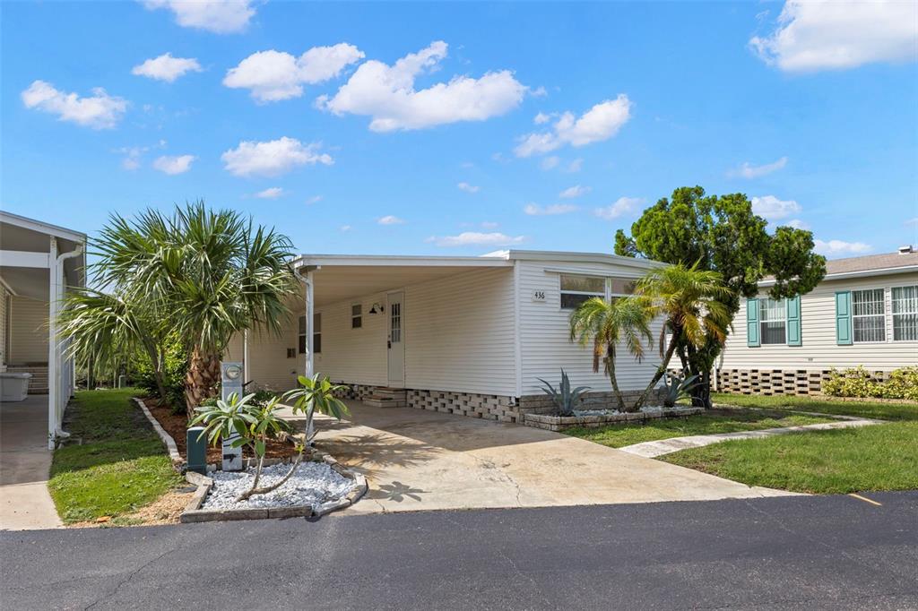 A white mobile home with a carport, concrete driveway, and palm trees under a blue sky — 436 MOUNT OAK AVENUE NE UNIT 747, ST PETERSBURG, FL