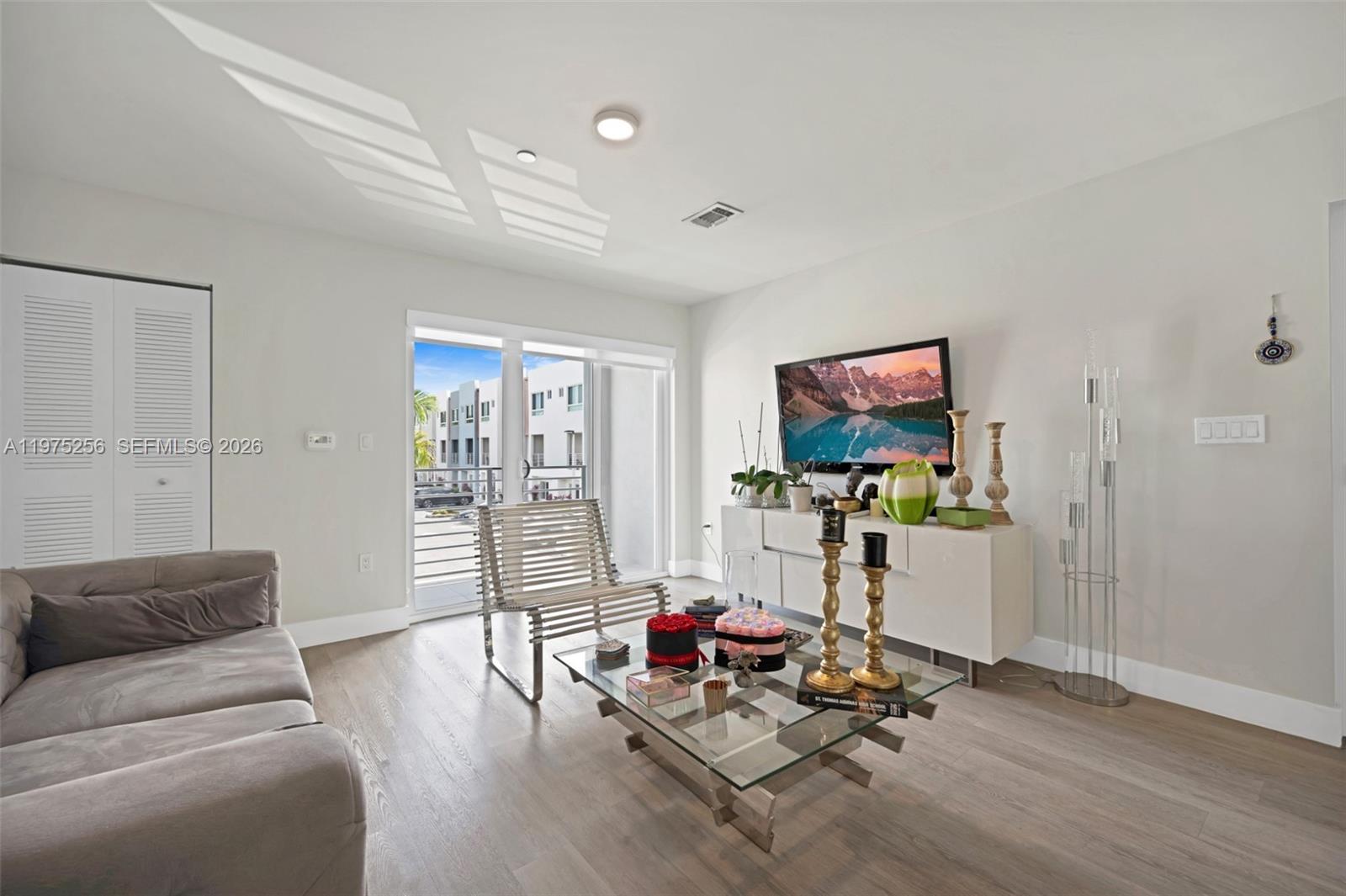 A modern living room features light wood floors, a glass coffee table, and a balcony view — 2535 NE 193rd St # 3209, Miami FL 33180, MIAMI, FL