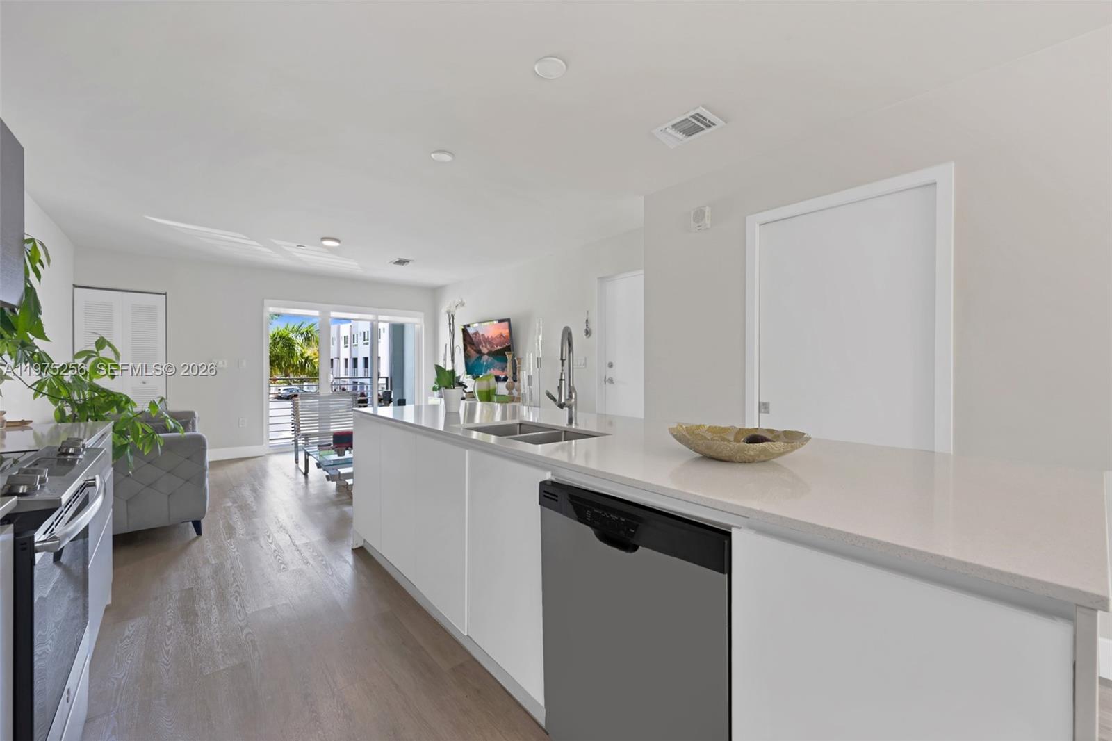 A modern kitchen with white cabinetry and quartz countertops overlooks a living area with balcony access — 2535 NE 193rd St # 3209, Miami FL 33180, MIAMI, FL