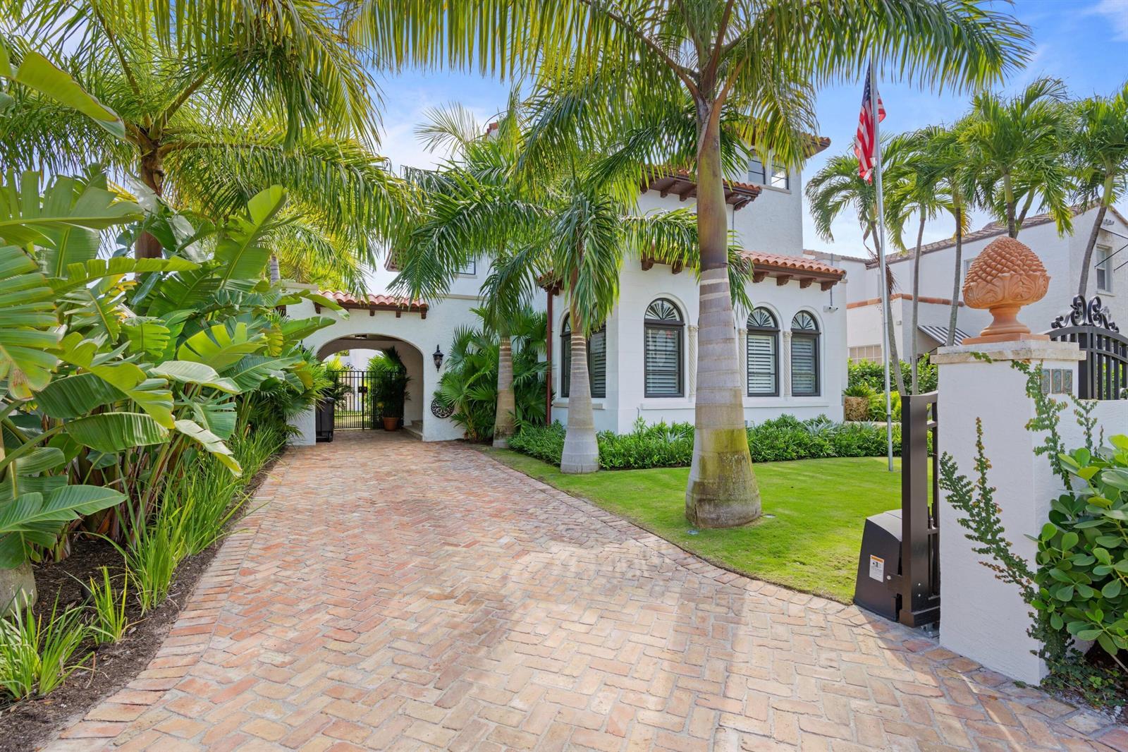 A white Mediterranean-style house with a brick driveway, palm trees, and an American flag — 112 Roosevelt Place, West Palm Beach FL 33405, WEST PALM BEACH, FL