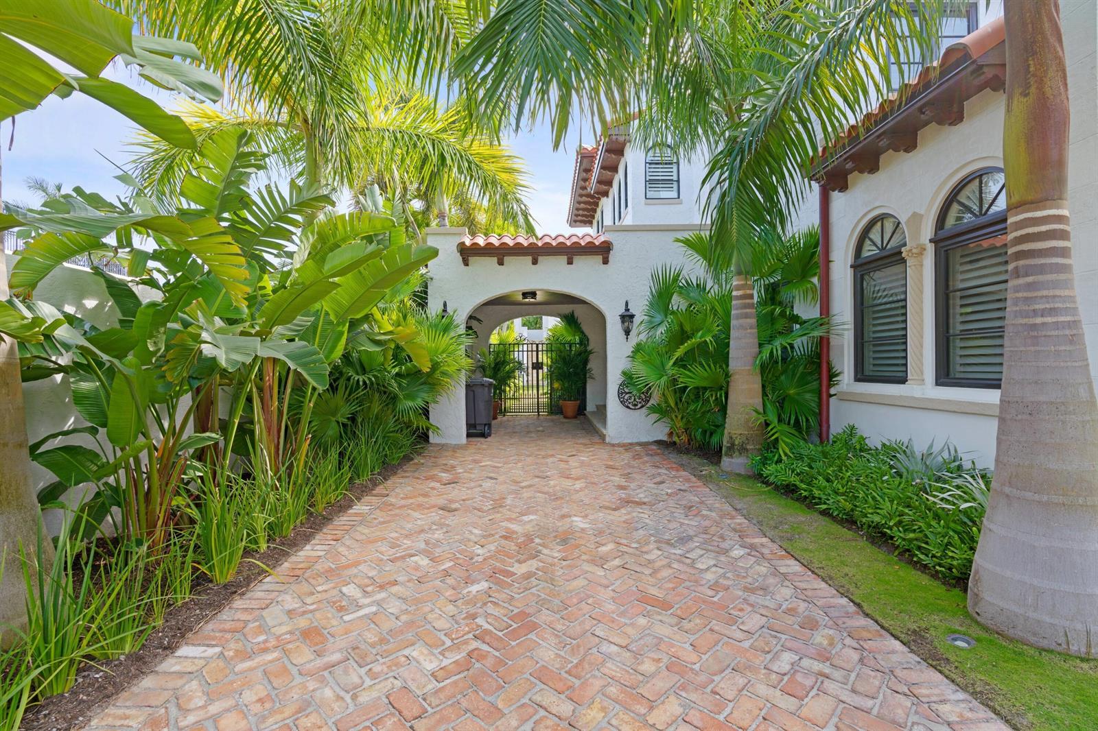 A brick driveway leads to a gated archway beside a white house with palm trees — 112 Roosevelt Place, West Palm Beach FL 33405, WEST PALM BEACH, FL