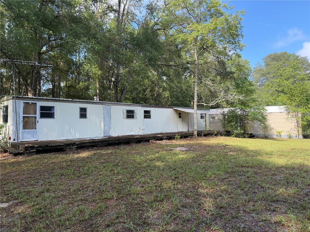 An exterior view of two connected mobile homes with a wooden deck in a wooded area — 9730 NE STATE ROAD 24, ARCHER, FL