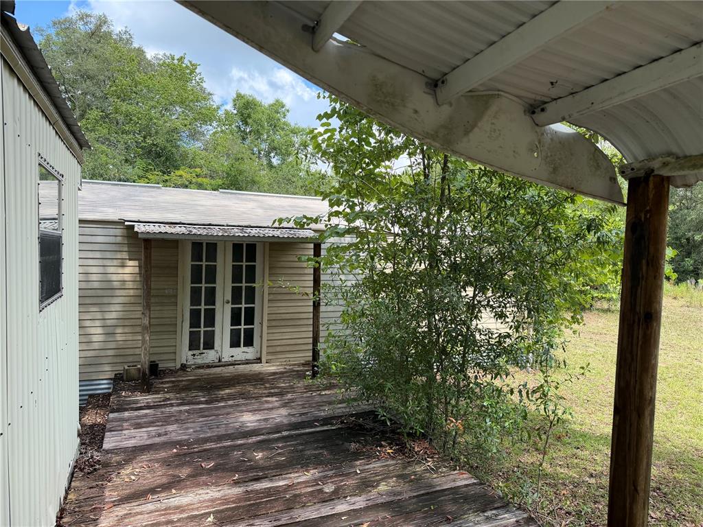 A wooden deck leads to a set of French doors on a light-colored mobile home — 9730 NE STATE ROAD 24, ARCHER, FL