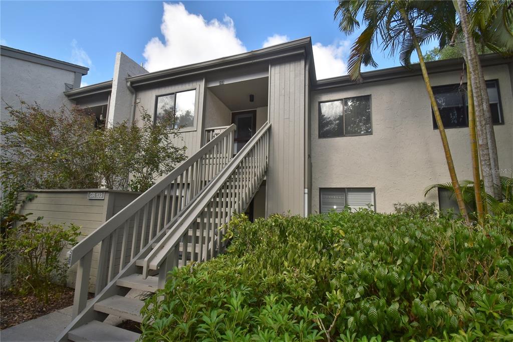 An exterior view of a two-story apartment building with a wooden staircase leading to an entrance — 1508 PELICAN COVE ROAD UNIT GR233, SARASOTA, FL