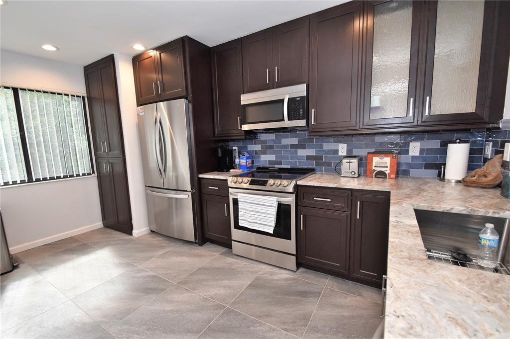 A kitchen features dark wood cabinets, stainless steel appliances, blue tile backsplash, and stone countertops — 1508 PELICAN COVE ROAD UNIT GR233, SARASOTA, FL