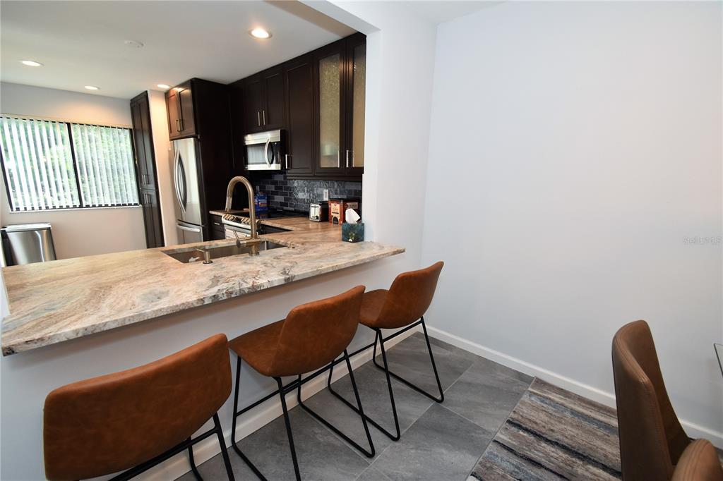 A kitchen features dark wood cabinets, granite countertops, a breakfast bar, and three brown stools — 1508 PELICAN COVE ROAD UNIT GR233, SARASOTA, FL