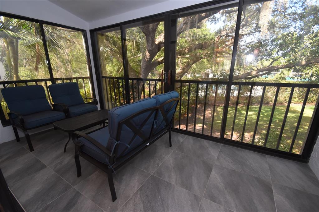 A screened-in porch features gray tile flooring, patio furniture, and views of trees outside — 1508 PELICAN COVE ROAD UNIT GR233, SARASOTA, FL