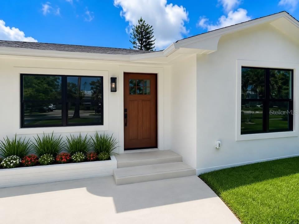 A white house exterior features a wooden front door, black-framed windows, and a concrete planter — 3219 E DE BAZAN AVENUE, ST PETERSBURG, FL