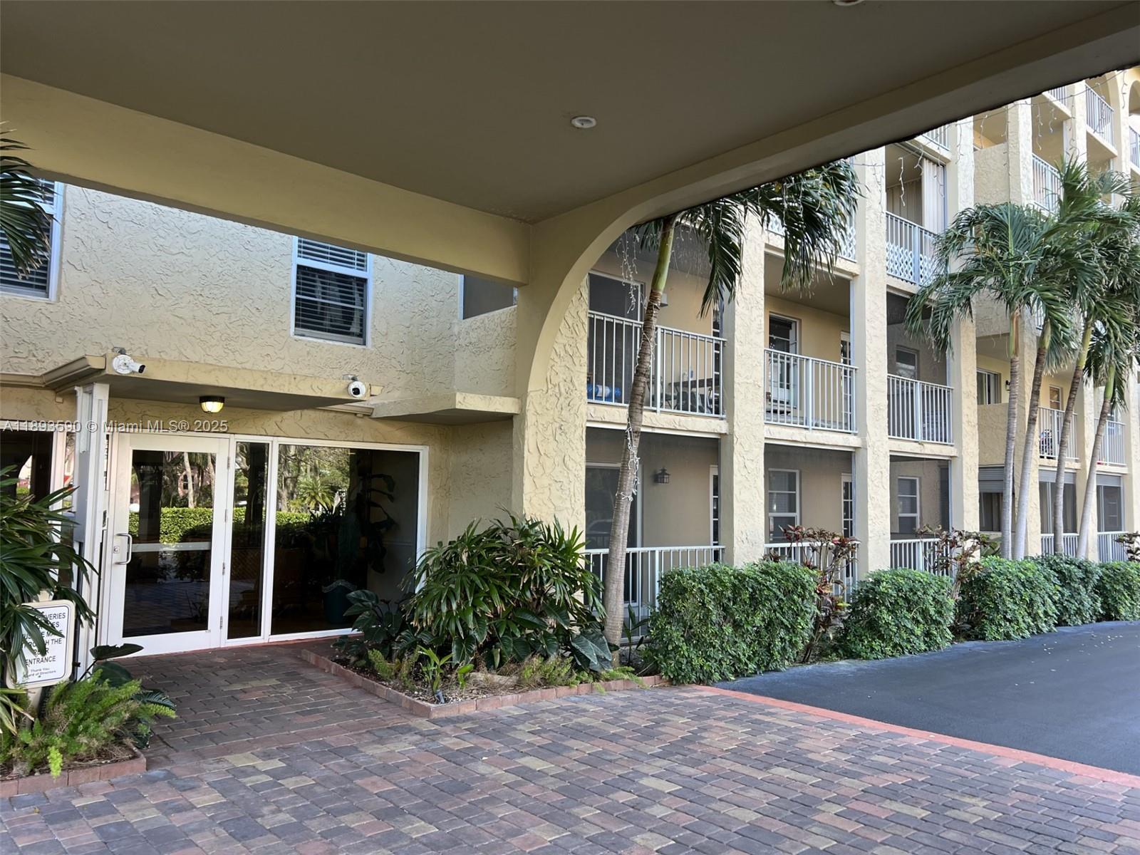 The exterior of a multi-story apartment building features a covered entrance and paved driveway — 950 Ponce De Leon Rd # 2100, Boca Raton FL 33432, BOCA RATON, FL