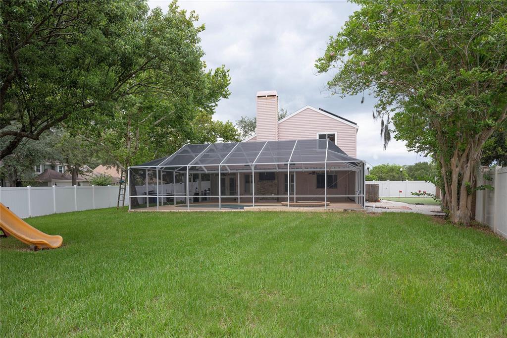 A backyard view of a two-story house with a screened-in pool enclosure and a slide — 9609 FREDERICKSBURG ROAD, TAMPA, FL