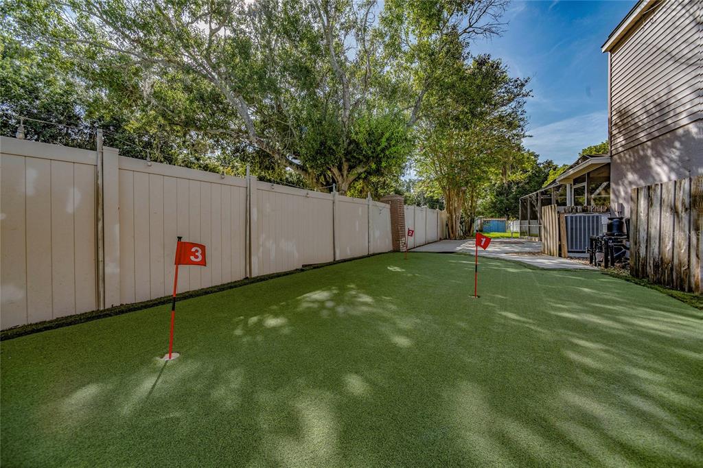 A backyard putting green with three numbered flags sits beside a house and vinyl fence — 9609 FREDERICKSBURG ROAD, TAMPA, FL