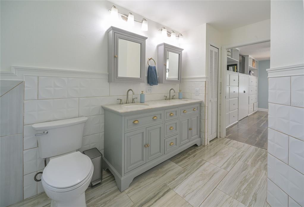 A bathroom features a double vanity with gray cabinets, white tiled walls, and wood-look flooring — 9609 FREDERICKSBURG ROAD, TAMPA, FL