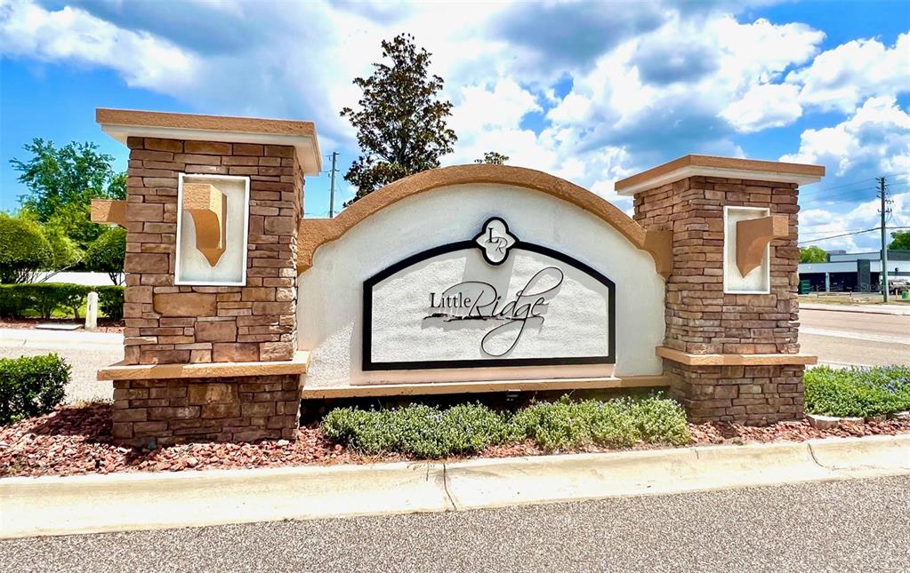 A stone monument sign for Little Ridge stands outdoors under a cloudy blue sky — 8427 BLUE ROCK DRIVE, NEW PORT RICHEY, FL