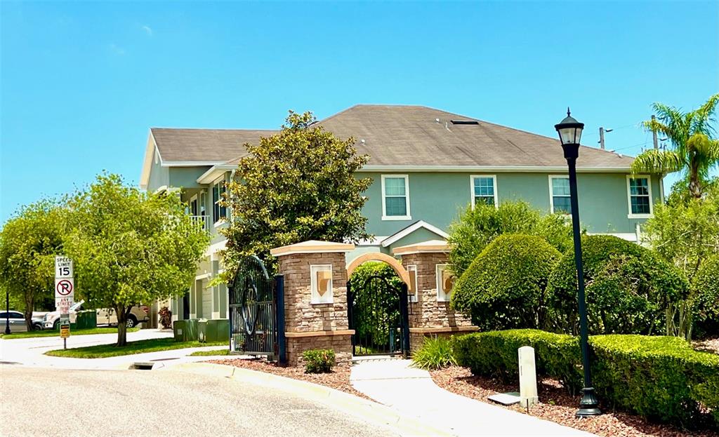 A two-story building with a stone-accented gated entrance and a speed limit sign — 8427 BLUE ROCK DRIVE, NEW PORT RICHEY, FL