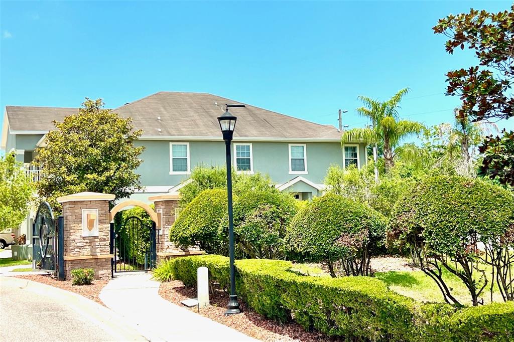A two-story light green house features a stone-pillared gate and manicured landscaping — 8427 BLUE ROCK DRIVE, NEW PORT RICHEY, FL