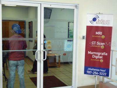 A person stands before the glass entrance doors of a radiology office with a standing sign — 3 PR-3 KM 19.9, BARRIO DOS CUERDAS, CANOVANAS, PR