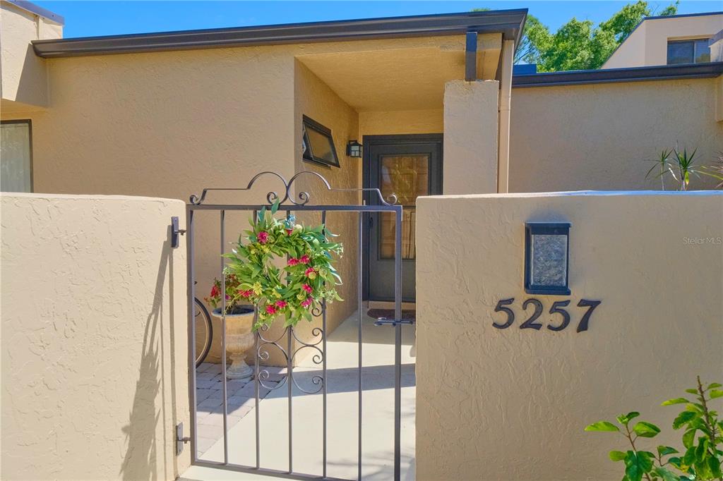 A tan stucco exterior features a gated courtyard entrance with a decorative wreath and house numbers — 5257 MYRTLE WAY UNIT 29, SARASOTA, FL