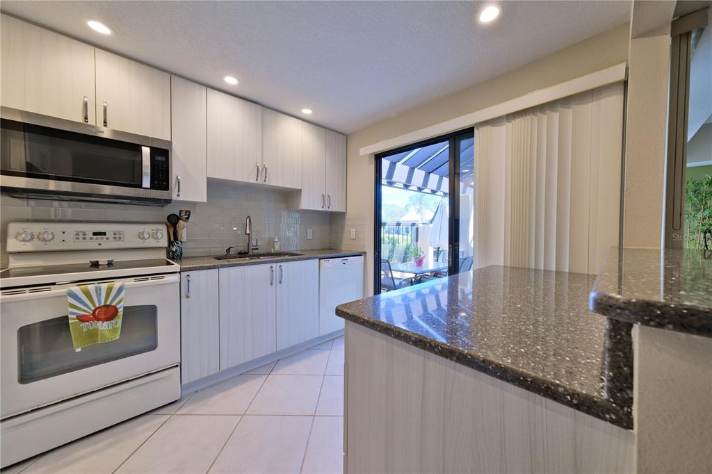 A kitchen with white cabinets, dark speckled countertops, white appliances, and a sliding glass door — 5257 MYRTLE WAY UNIT 29, SARASOTA, FL