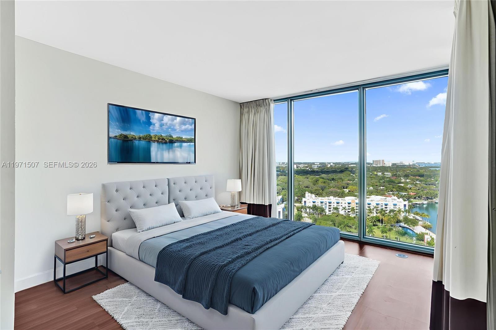 A bedroom features a tufted gray bed, wood flooring, and floor-to-ceiling windows with water views — 601 NE 36th St # 1908, Miami FL 33137, MIAMI, FL