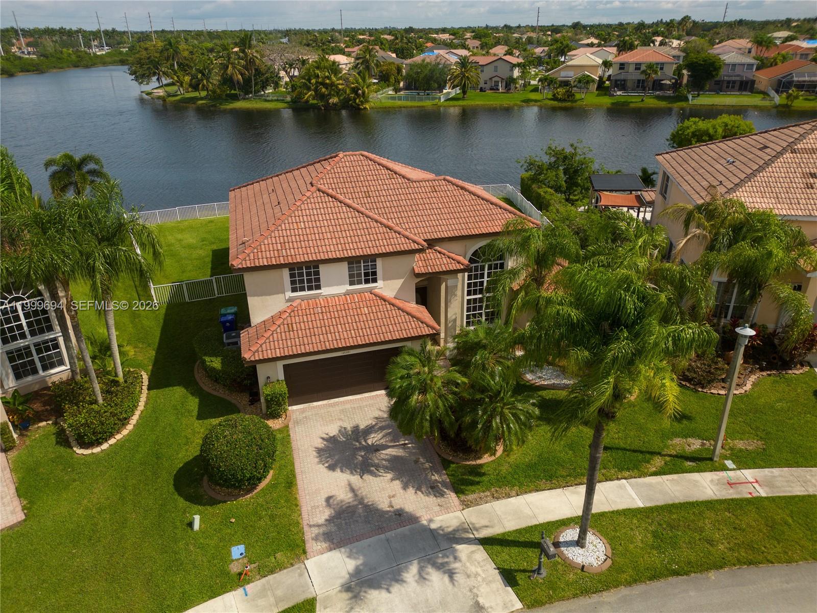 An aerial view shows a two-story house with a tile roof, driveway, and backyard lake — 18281 SW 22nd St, Miramar FL 33029, MIRAMAR, FL