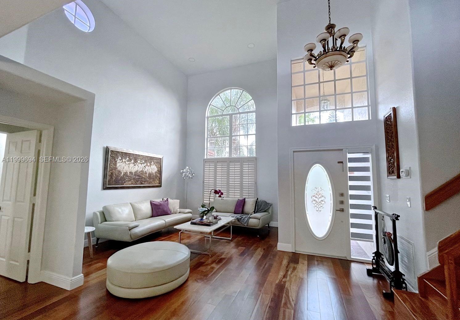 A high-ceilinged living room features hardwood floors, a white sofa set, and a large window — 18281 SW 22nd St, Miramar FL 33029, MIRAMAR, FL